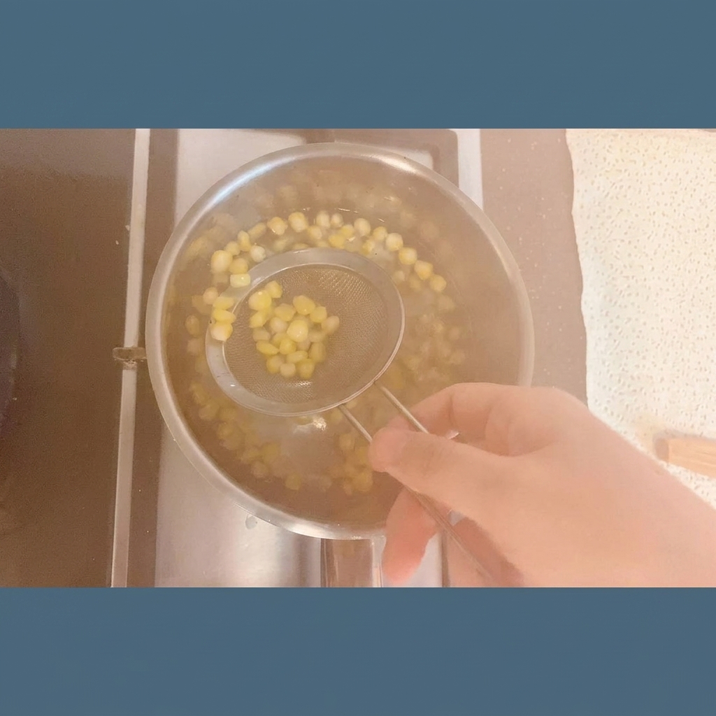Granos de maíz de color amarillo brillante siendo extraídos de una olla de agua humeante con un colador de malla de acero inoxidable.