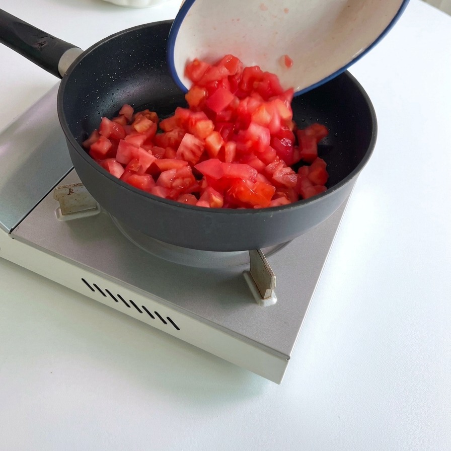 Tomates rojos cortados en cubos vertiéndose desde un tazón de cerámica blanca en una sartén negra caliente.