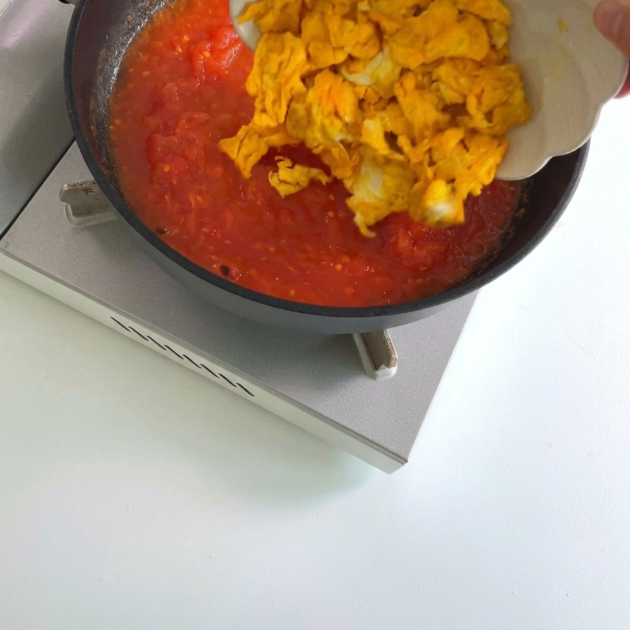 Trozos de huevo revuelto amarillo cocido añadiéndose a una sartén que contiene una salsa de tomate roja hirviendo a fuego lento.