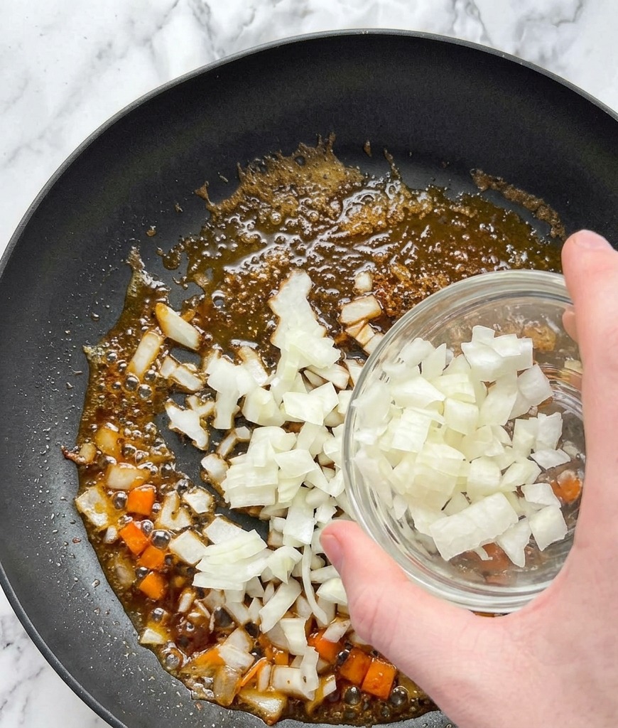Cebolla blanca picada cayendo desde un bol de vidrio a una sartén con aceite y los jugos del salmón.