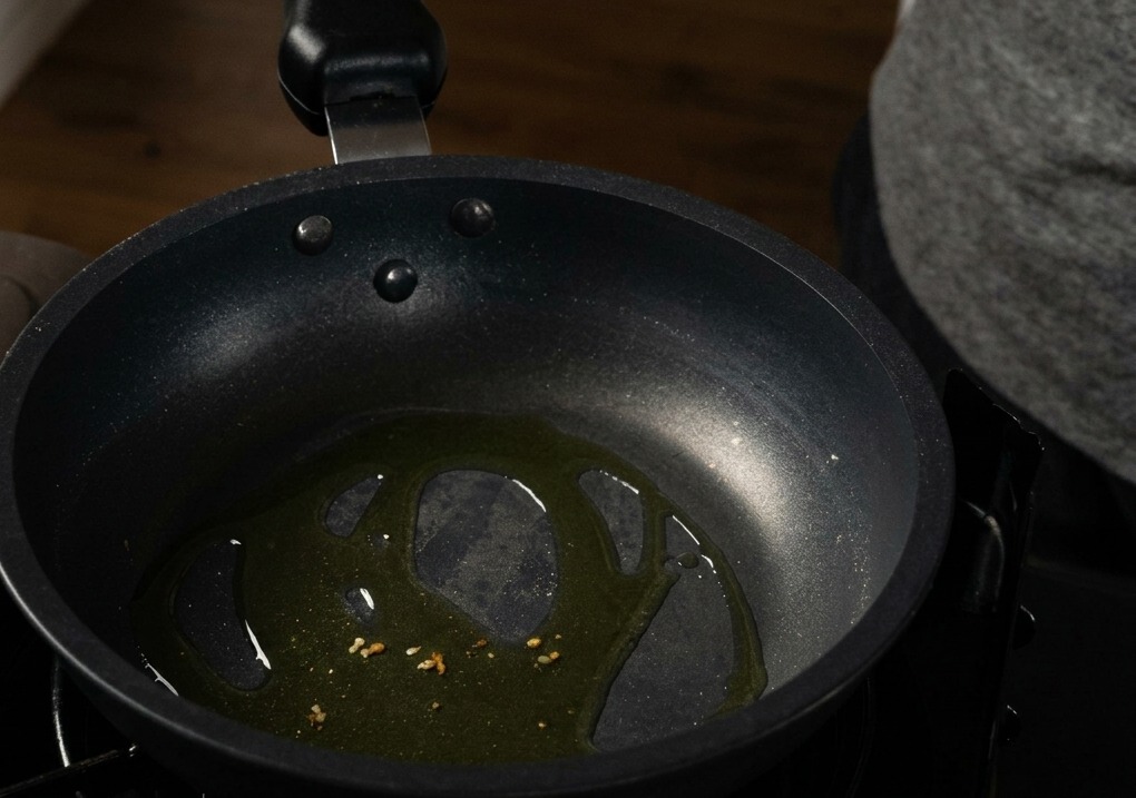 Trozos de ajo picado sofriéndose en aceite de oliva en el fondo de una sartén antiadherente negra.