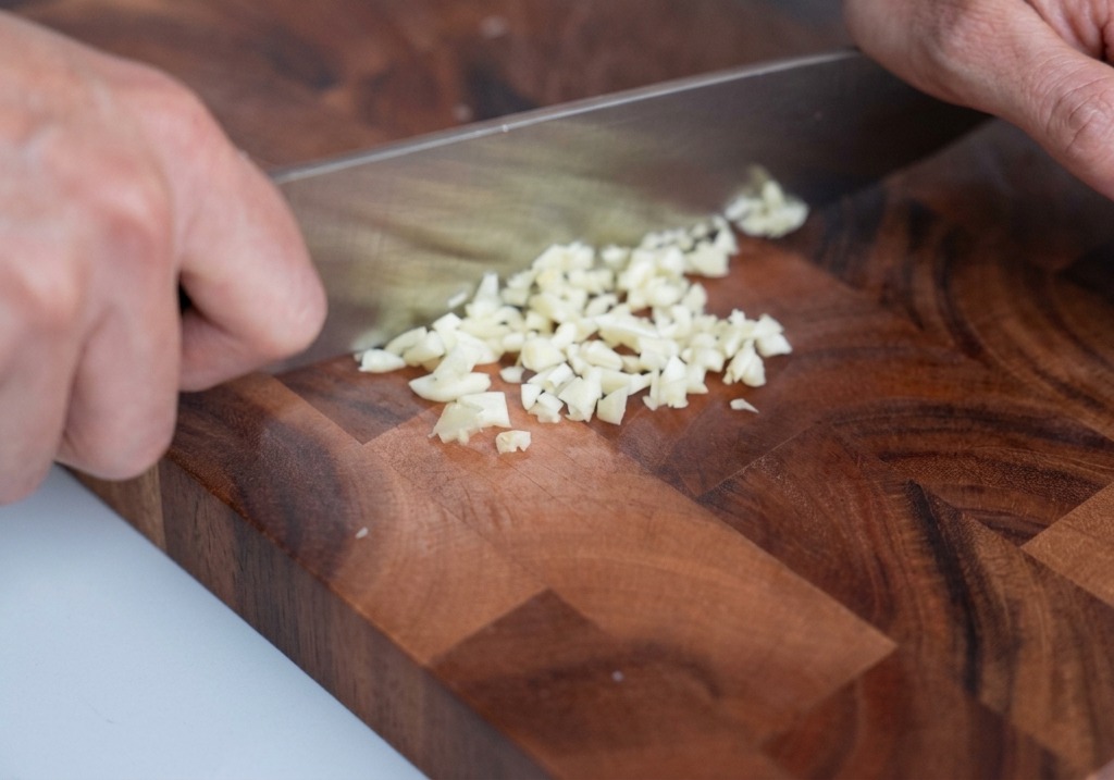 Ajo finamente picado sobre una tabla de cortar de madera con un cuchillo de chef cerca.