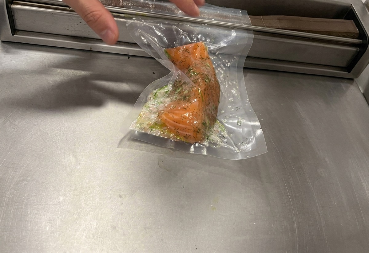 Una máquina de sellado al vacío extrayendo el aire de una bolsa plástica que contiene un filete de salmón cubierto de hierbas.