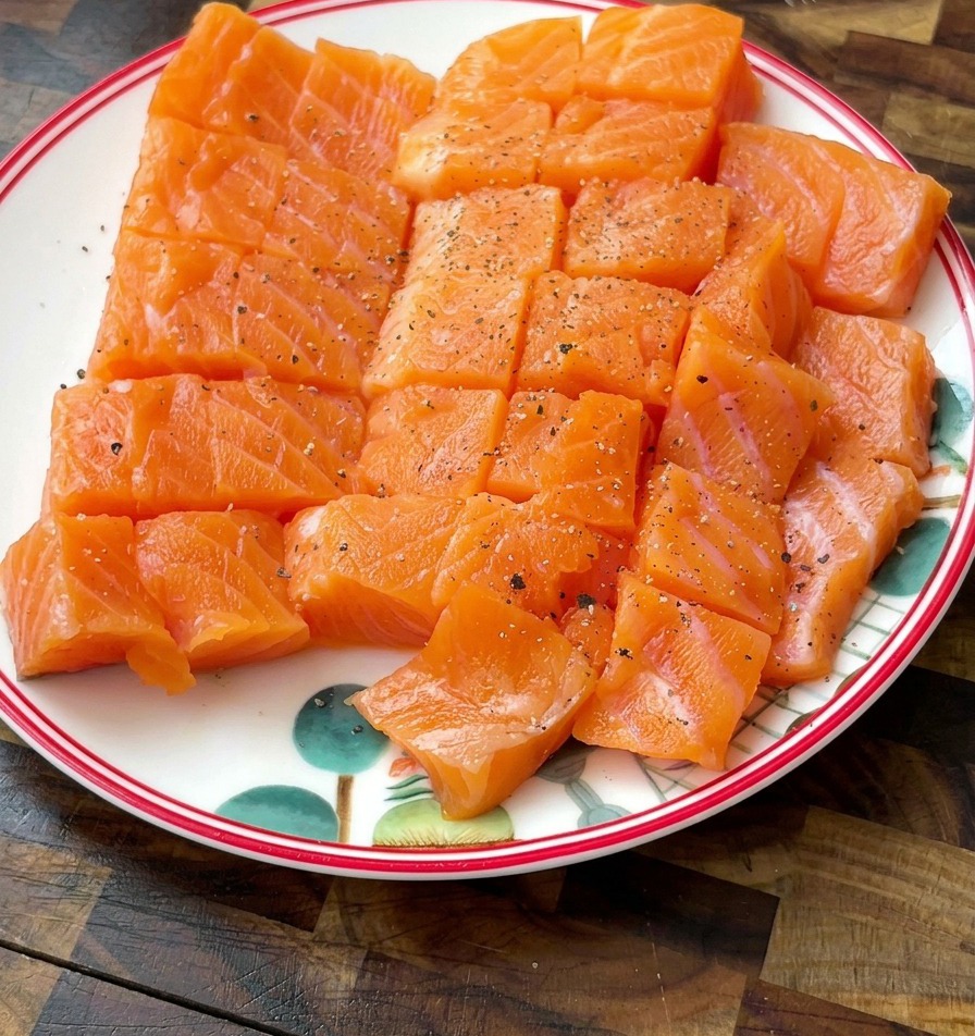 Dados de salmón en un plato blanco con motas visibles de pimienta negra y sal.