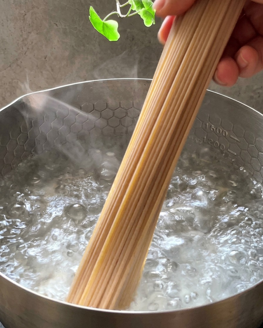 Un manojo de espaguetis integrales secos introduciéndose en una olla de acero inoxidable con agua hirviendo.