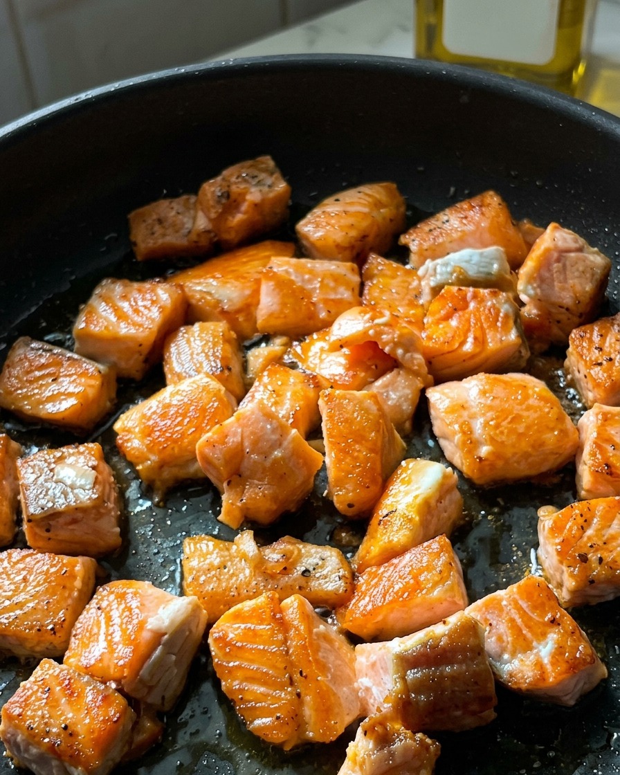Trozos de salmón en dados en una sartén con una costra crujiente y dorada en sus superficies selladas.