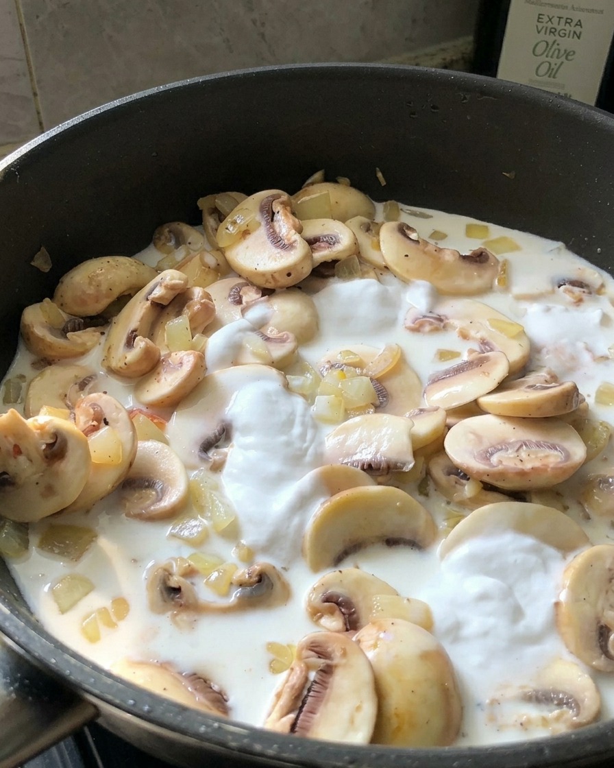 Una persona probando una salsa de crema blanca con una cuchara pequeña directamente de una sartén negra con champiñones.