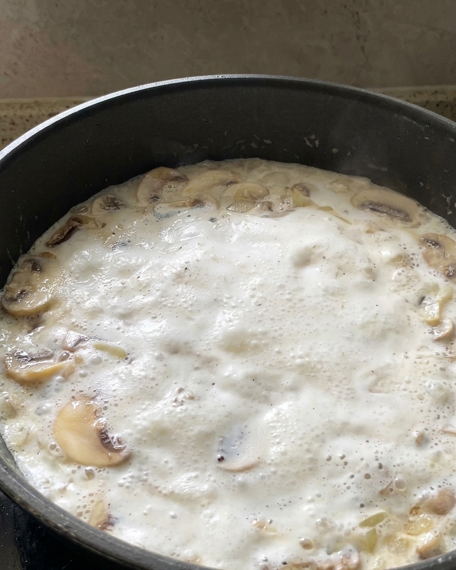 Hojas de espinaca verdes frescas añadiéndose a una salsa de crema de champiñones que burbujea en una sartén.