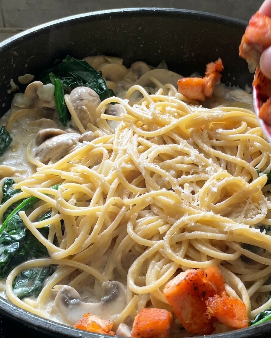 Dados de salmón sellados y dorados colocándose encima de la pasta cremosa terminada con espinacas.