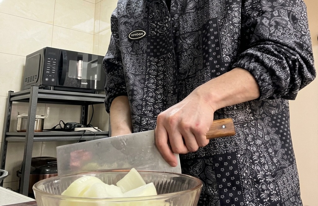 Manos sosteniendo un cuchillo grande picando una cebolla en una tabla de cortar de madera.