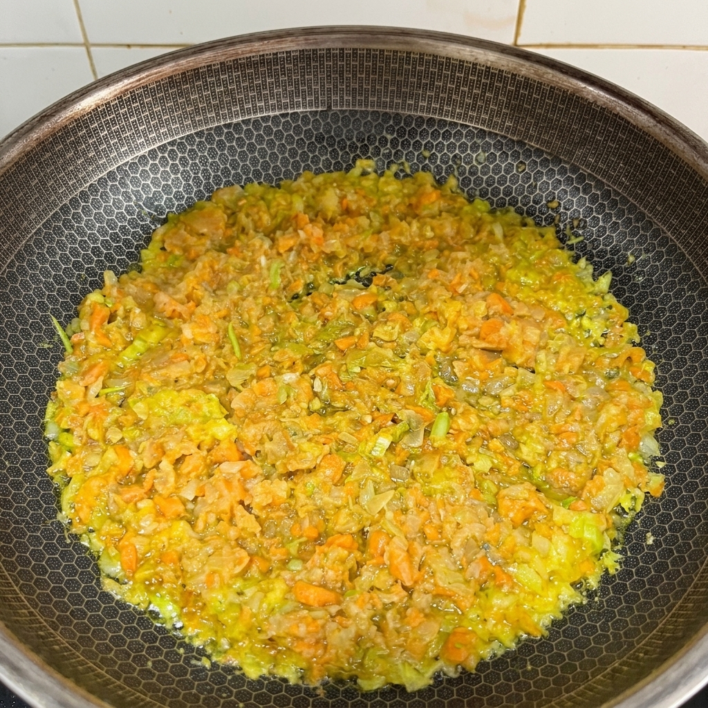 Zanahorias, apio y cebollas finamente picados sofriéndose en una sartén con mantequilla derretida.