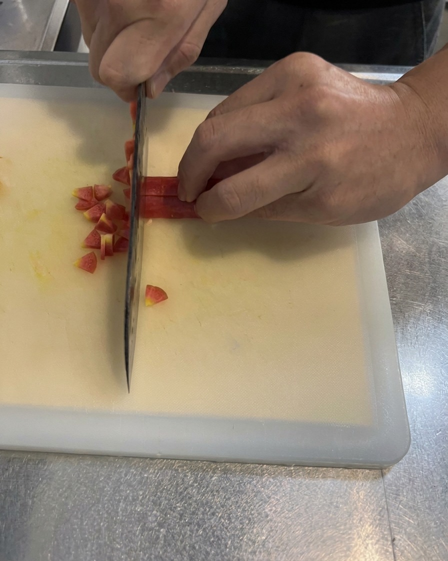 Manos cortando una zanahoria brillante en cubos pequeños y uniformes sobre una tabla de cortar blanca con un cuchillo de cocina.