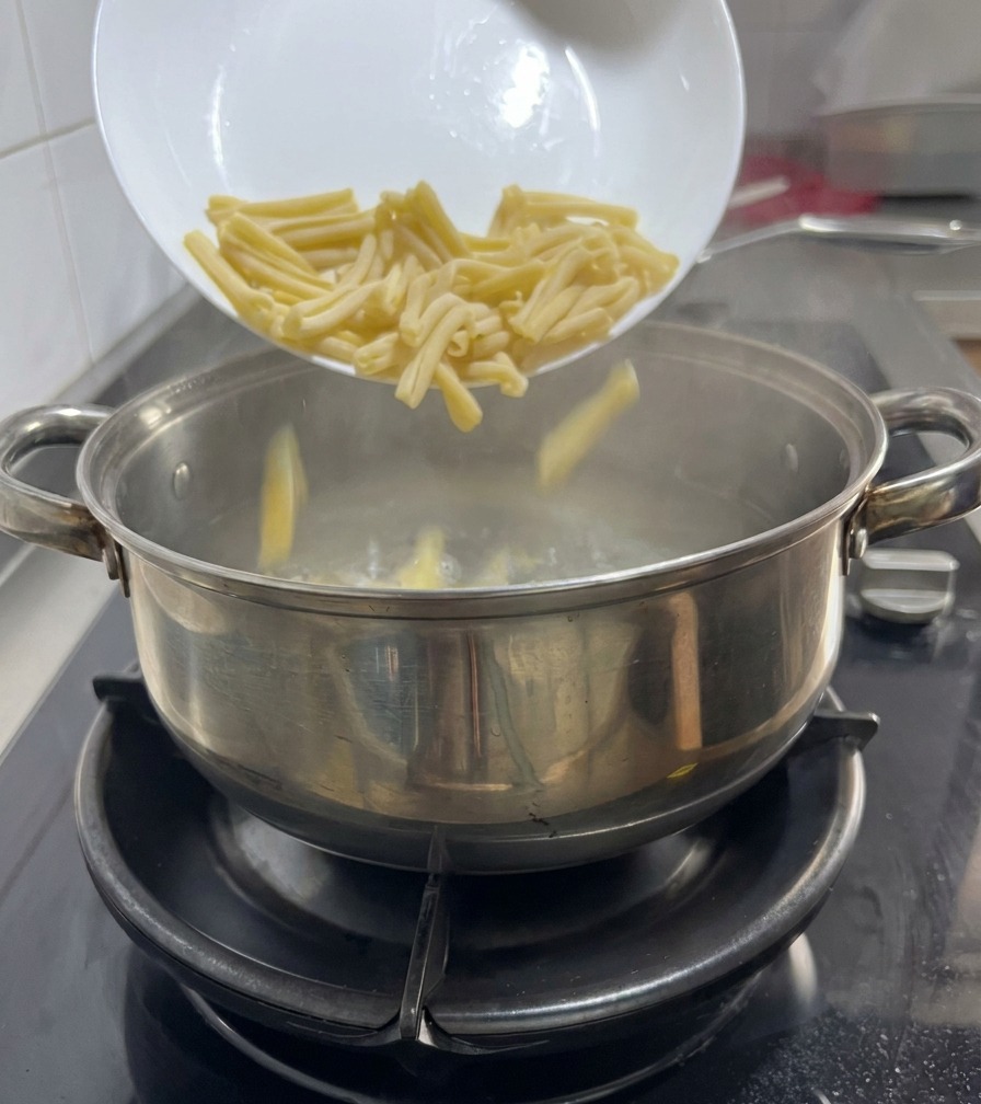 Pasta Casarecce cayendo desde un plato blanco a una olla de agua hirviendo sobre una cocina de gas.