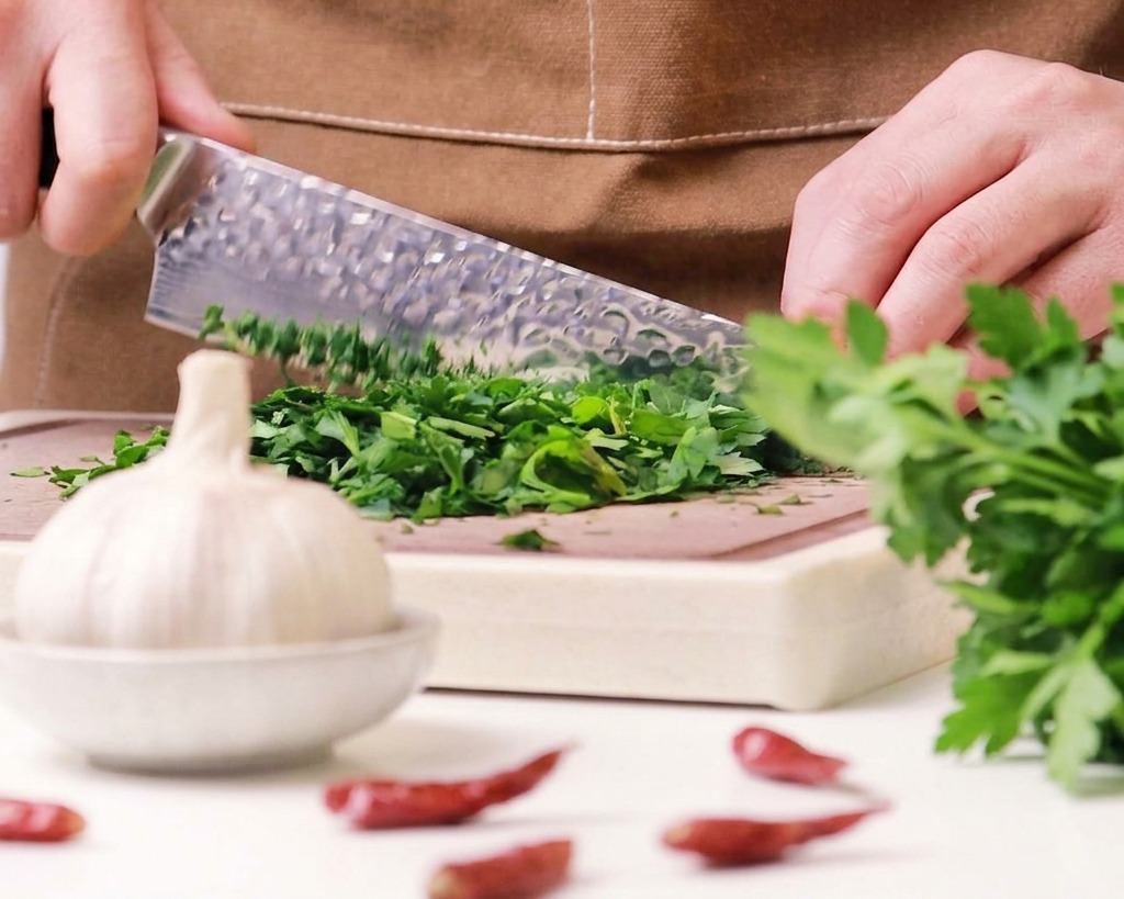 Primer plano de un chef usando un cuchillo con alvéolos para picar finamente un manojo de perejil verde fresco en una tabla de madera.