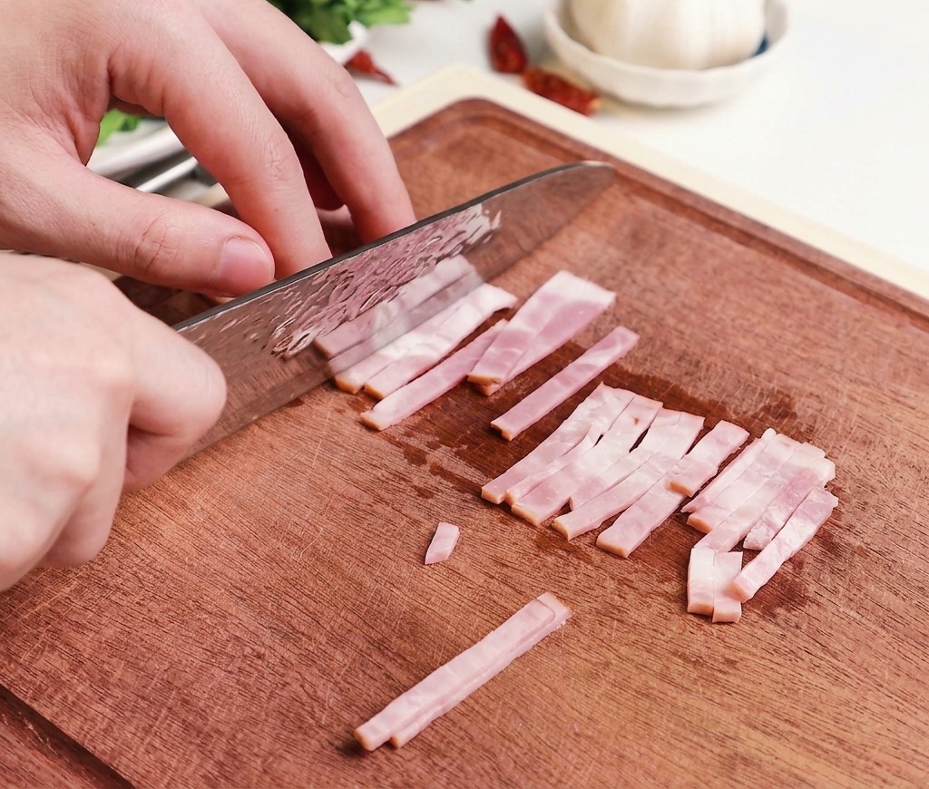 Manos usando un cuchillo de chef profesional para cortar tiras de bacón crudo y rosado en trozos pequeños y uniformes sobre una tabla de cortar de madera.