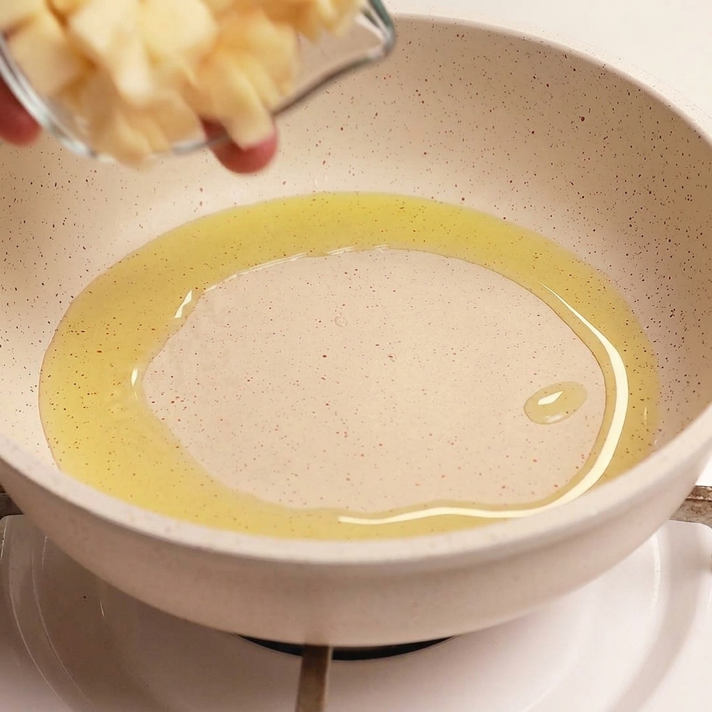Un pequeño cuenco de cristal vertiendo láminas finas y uniformes de ajo fresco en una sartén con aceite de oliva caliente y brillante.
