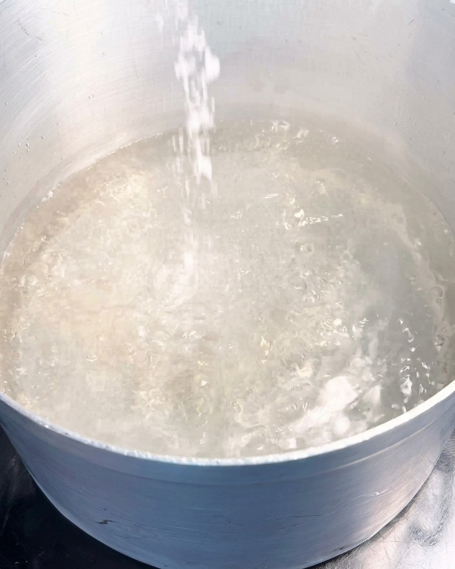 Un chorro de sal marina blanca vertiéndose en una olla de agua hirviendo a borbotones.