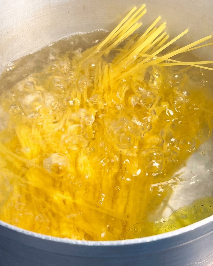 Un manojo de espaguetis amarillos secos sumergiéndose en una olla grande de agua hirviendo rápidamente.