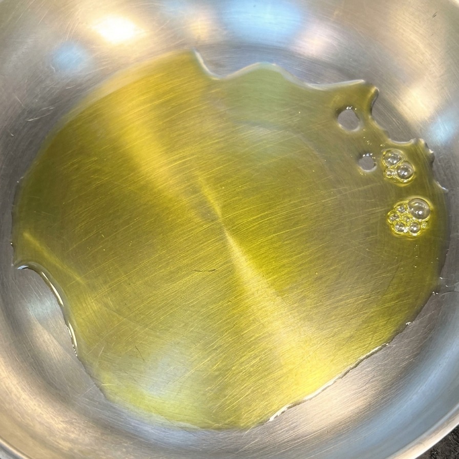 Un fondo de aceite de oliva amarillo vibrante cubriendo la base de una sartén limpia de acero inoxidable.