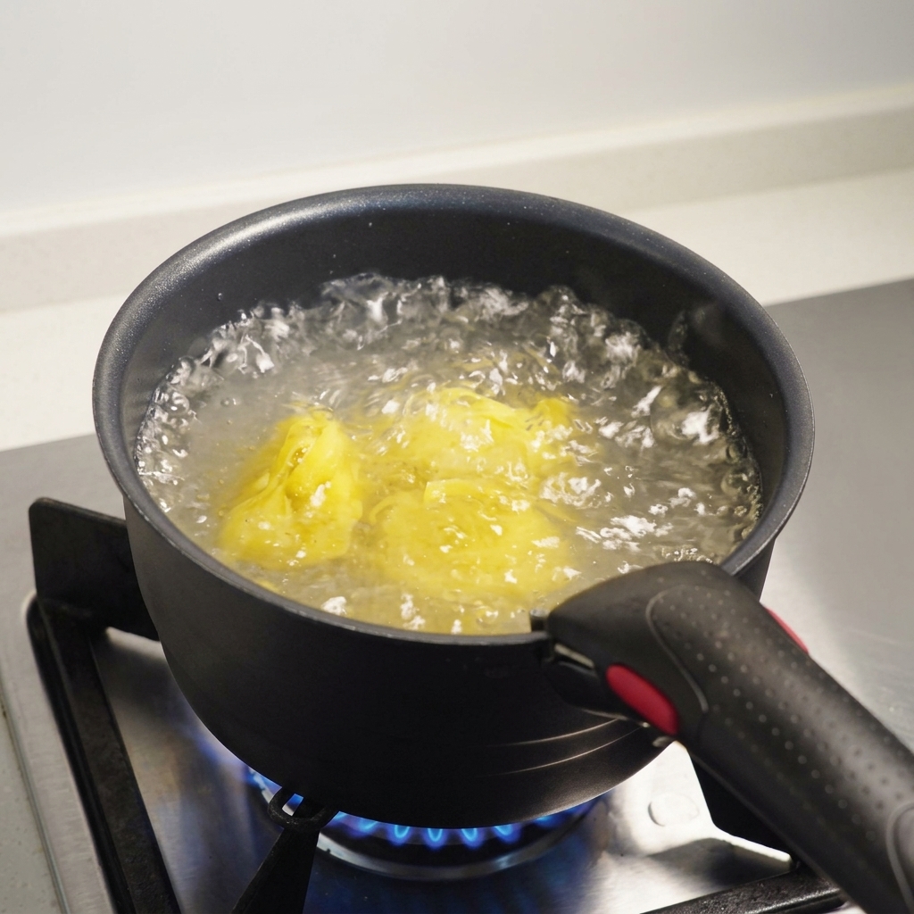 Pasta fettuccine sumergida en agua hirviendo con sal dentro de una olla oscura sobre una estufa de gas.