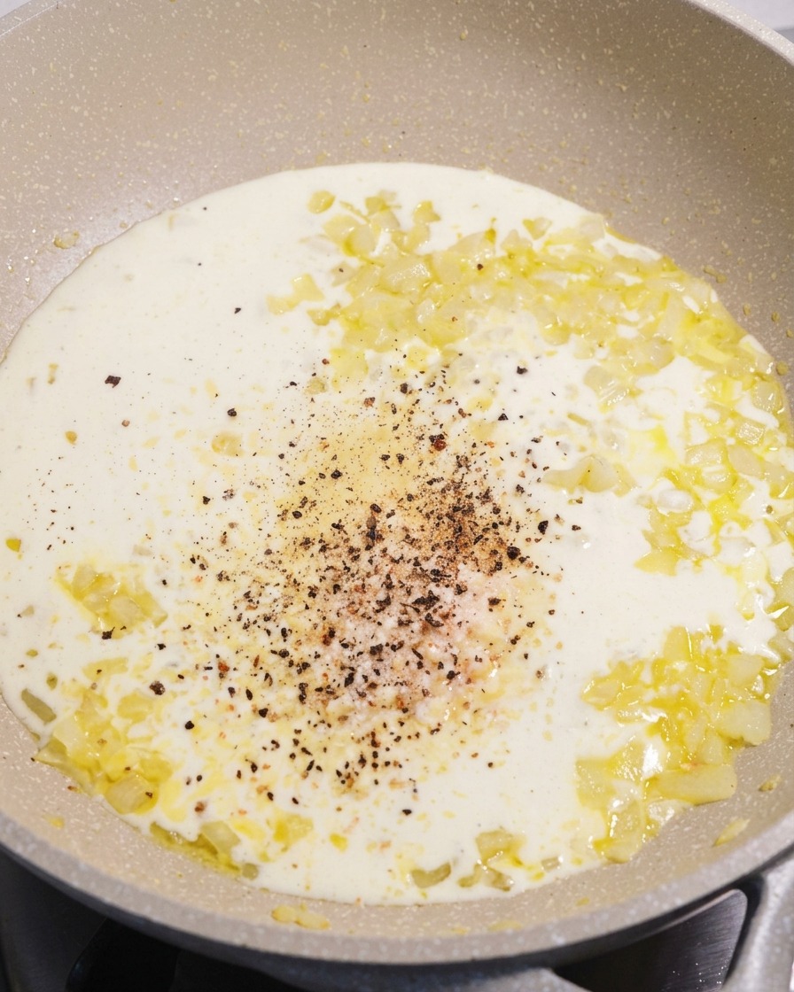Una sartén con salsa de crema blanca y suave, con una pila de pimienta negra recién molida y queso parmesano en el centro.
