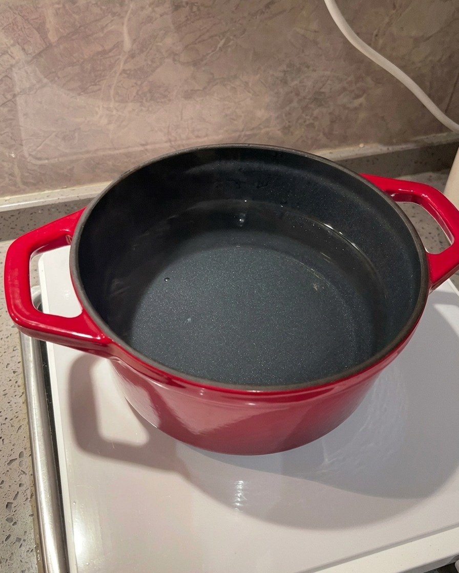 Primer plano de sal marina vertiéndose en una olla roja con agua sobre una estufa de inducción.