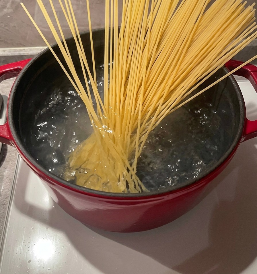 Un manojo de espaguetis secos colocándose en una olla de agua hirviendo con palillos de madera.