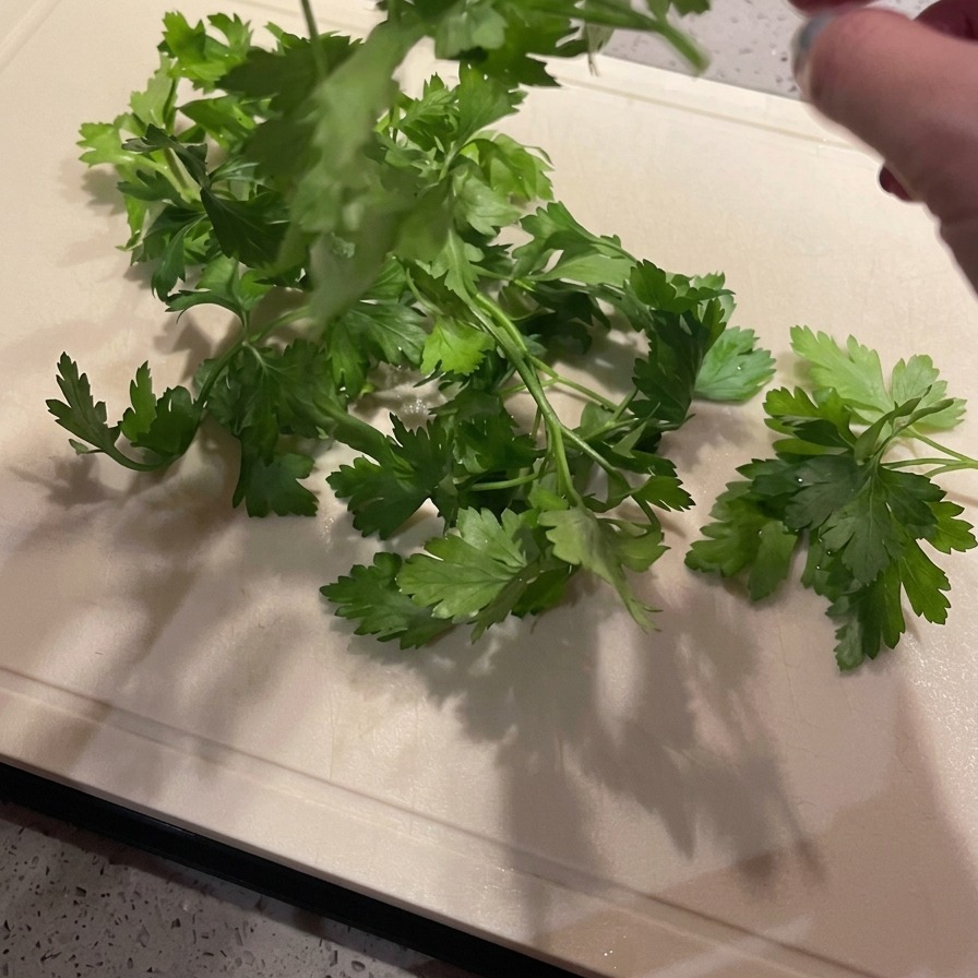 Manos separando hojas de perejil verde brillante de sus tallos sobre una tabla de cortar de color claro.