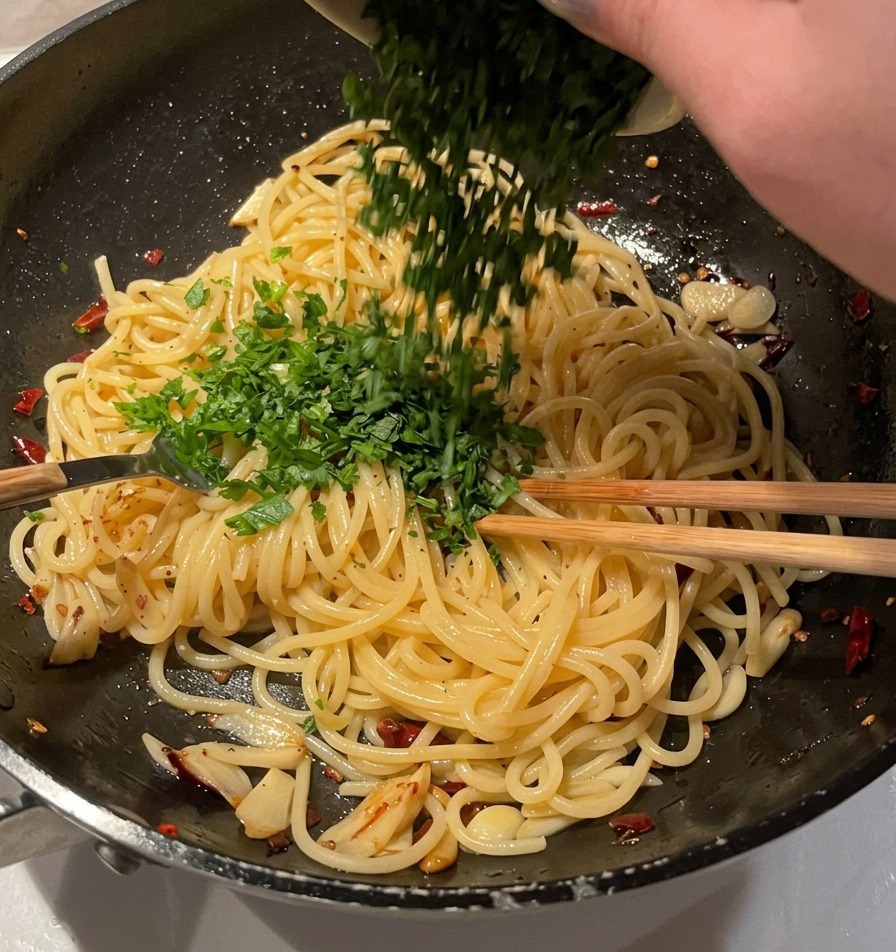 Un tazón de perejil fresco finamente picado vaciándose sobre una sartén de espaguetis con ajo y aceite.