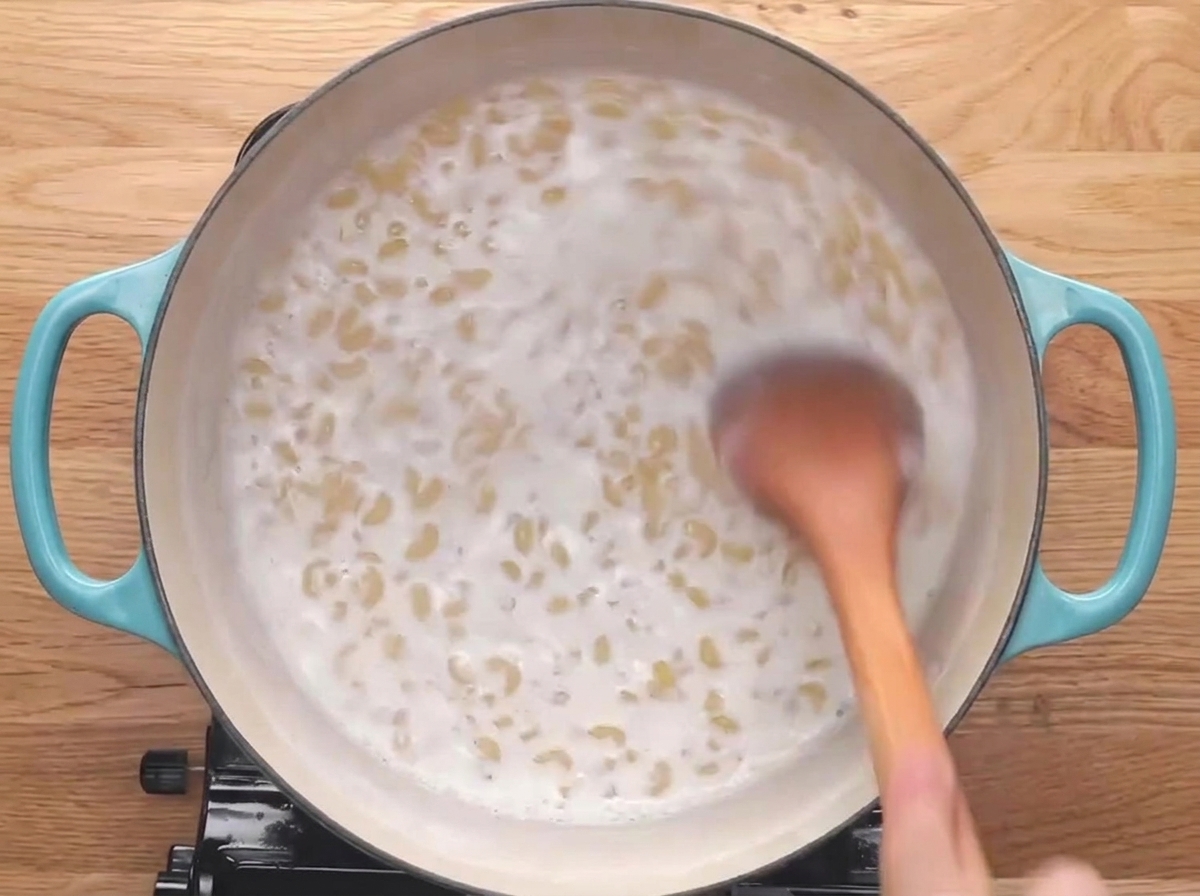 Una cuchara de madera removiendo los coditos de pasta mientras se cocinan en leche.