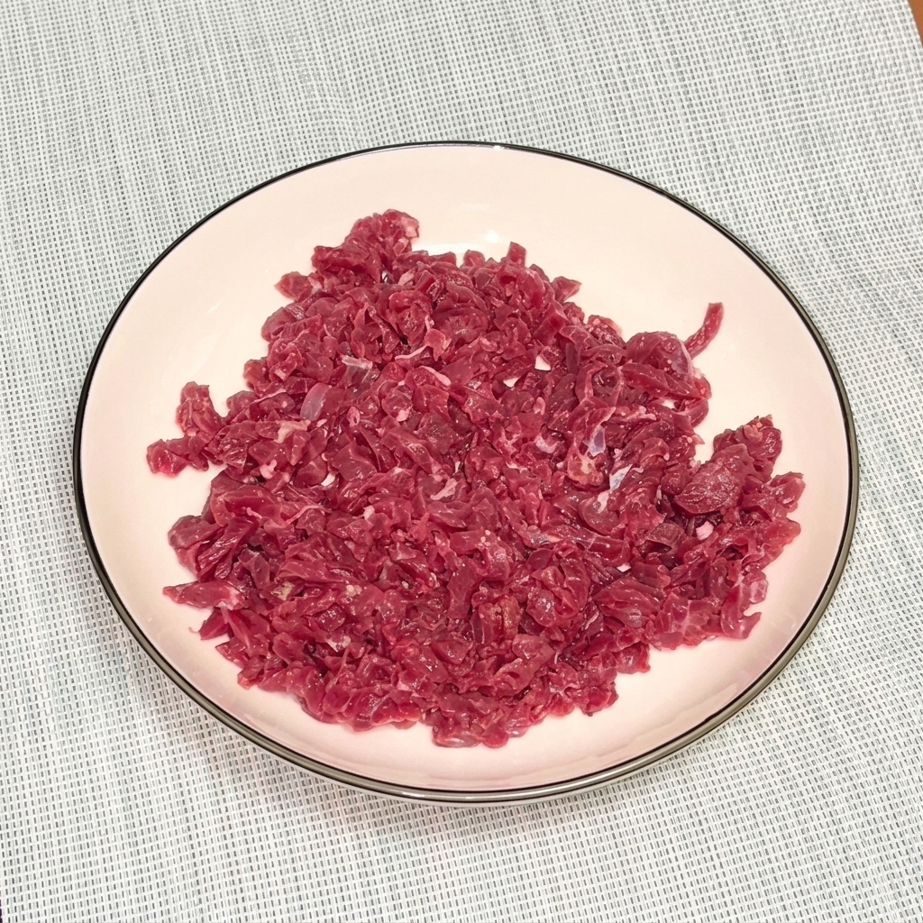 Carne picada cruda en un bol blanco con pimienta negra y aceite para marinar.