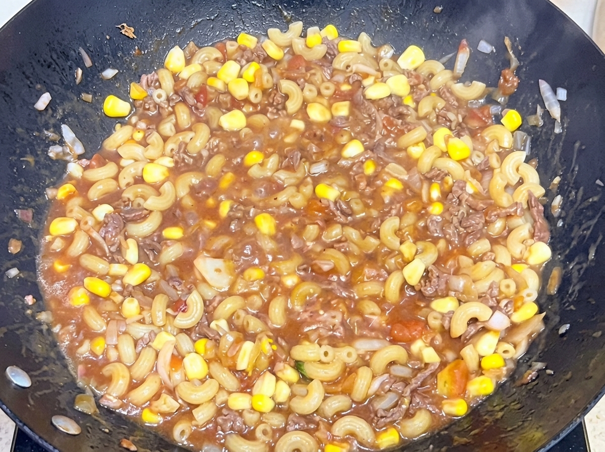 Macarrones cocidos mezclándose con la salsa de carne y tomate en un wok grande.