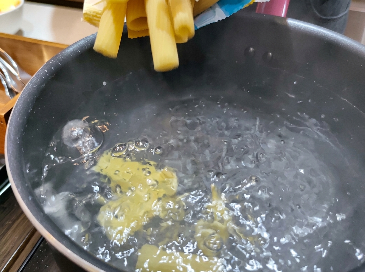 Pasta rigatoni seca y amarilla vertiéndose en una olla de agua hirviendo a borbotones.