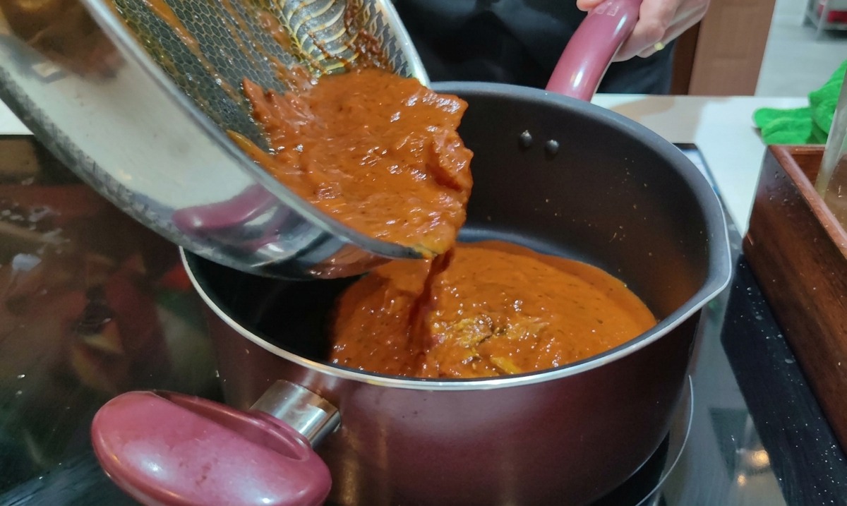 Virtiendo salsa amatriciana roja cocida desde una sartén en una olla con rigatoni hervidos.