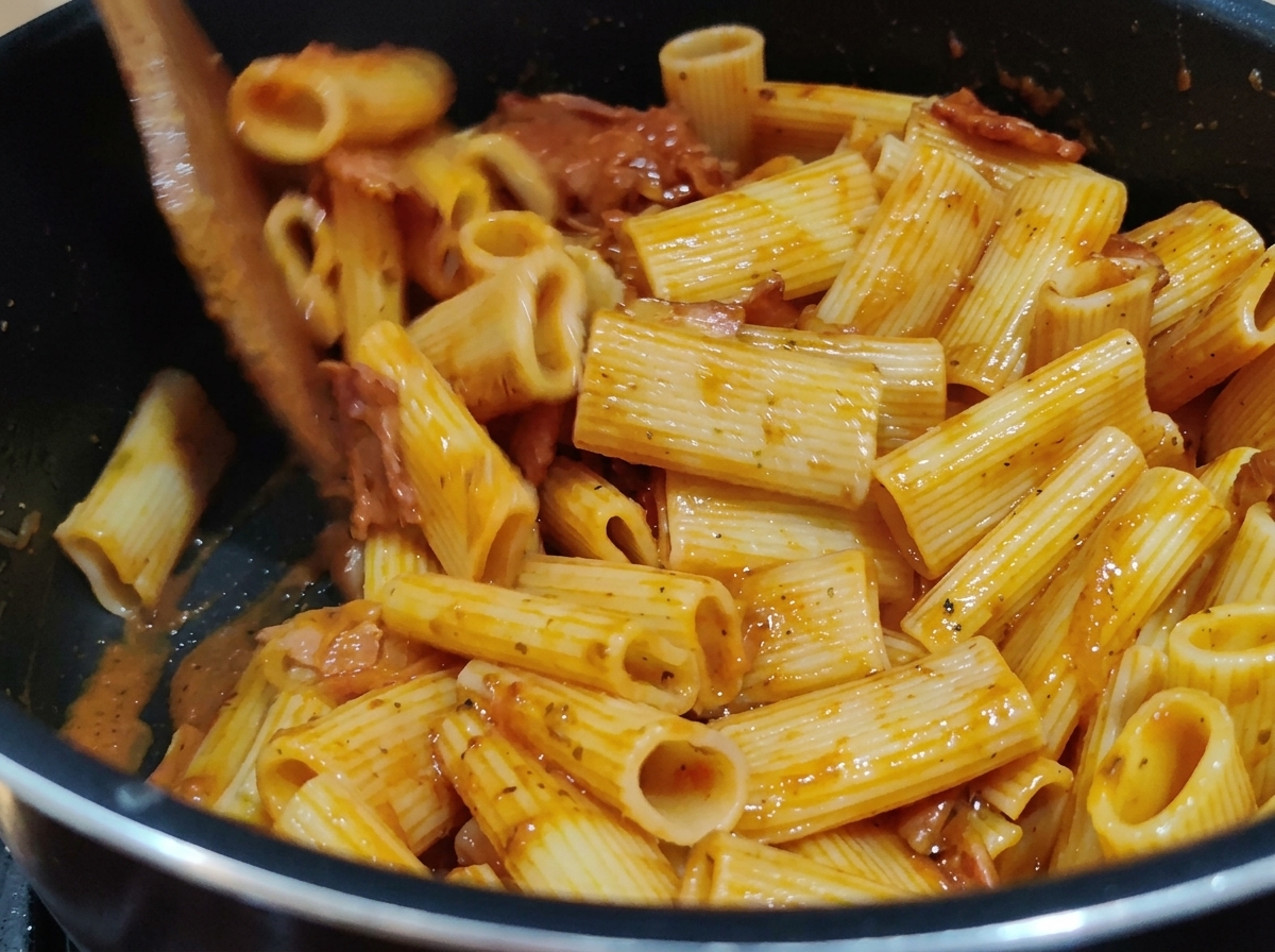 Removiendo pasta rigatoni con una rica salsa roja de tomate en una olla usando una espátula de madera.