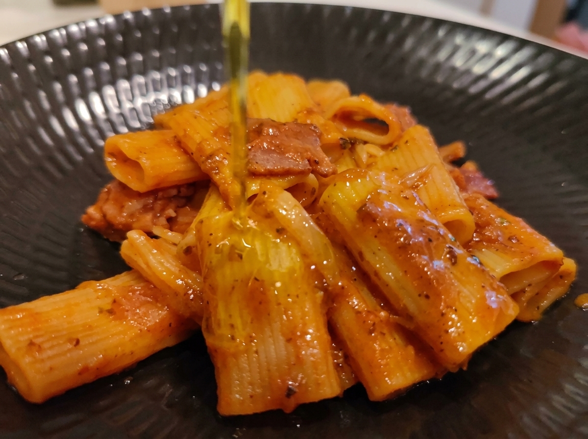 Virtiendo un chorrito de aceite de oliva virgen extra sobre una porción emplatada de rigatoni a la amatriciana.