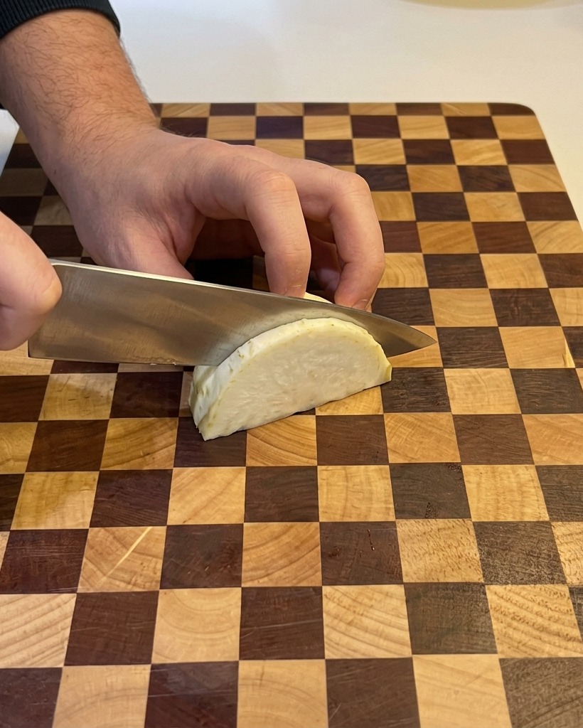 Una persona usando un cuchillo de chef para picar un trozo de cebolla blanca sobre una tabla de cortar de madera.
