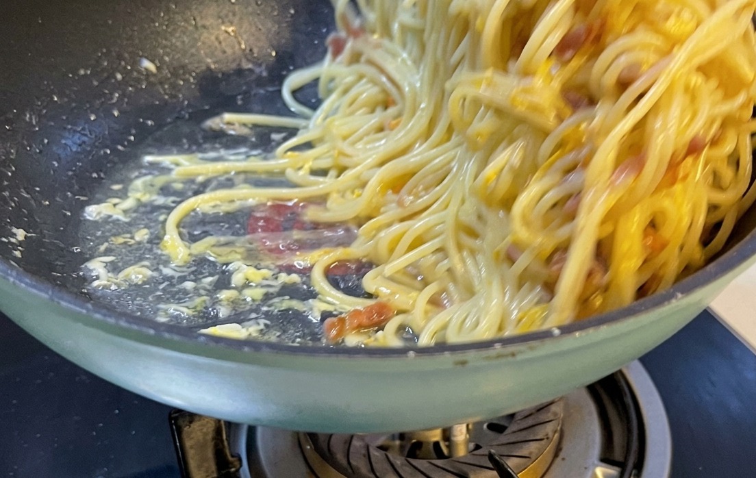 Una ración de espaguetis a la carbonara bellamente presentada en un plato de cerámica blanca coronada con queso rallado y pimienta.