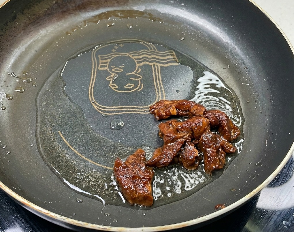 Tiras de cerdo marinadas salteándose en una sartén con aceite, mostrando un color marrón intenso y una superficie brillante.