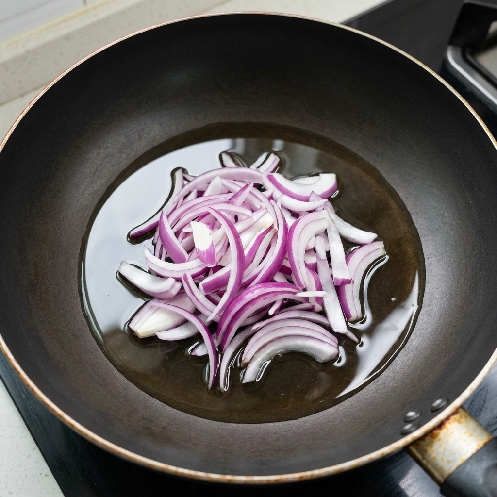 Cebolla morada en tiras salteándose en una capa ligera de aceite en una sartén negra.