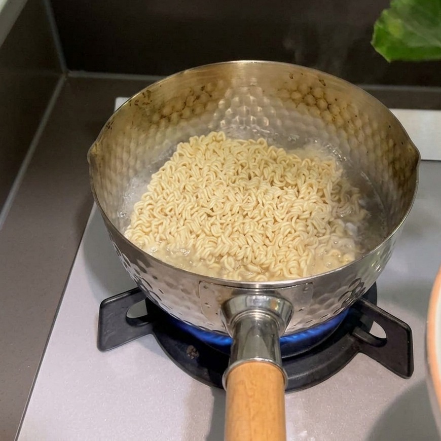 Una mano colocando hojas verdes de espinaca fresca sobre los fideos instantáneos que se cocinan en una olla hirviendo.