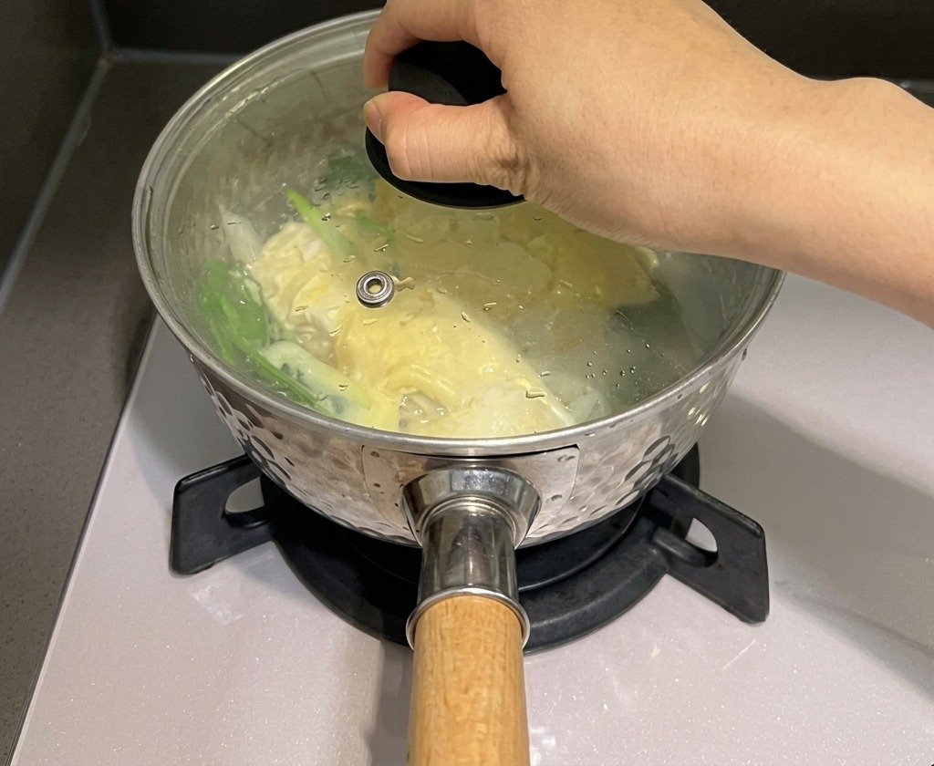 Una mano colocando una tapa de vidrio sobre una olla de fideos y queso para atrapar el vapor.