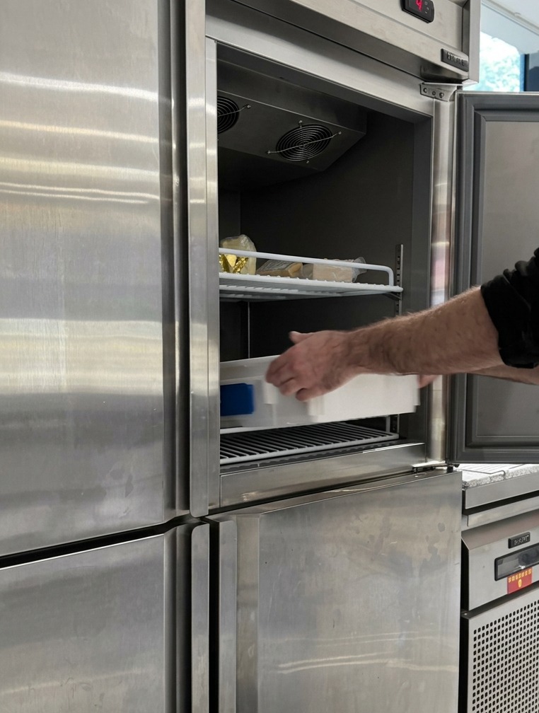 Una bandeja de fermentación blanca con bollos de masa redondos hundiéndose en el estante de un refrigerador industrial.
