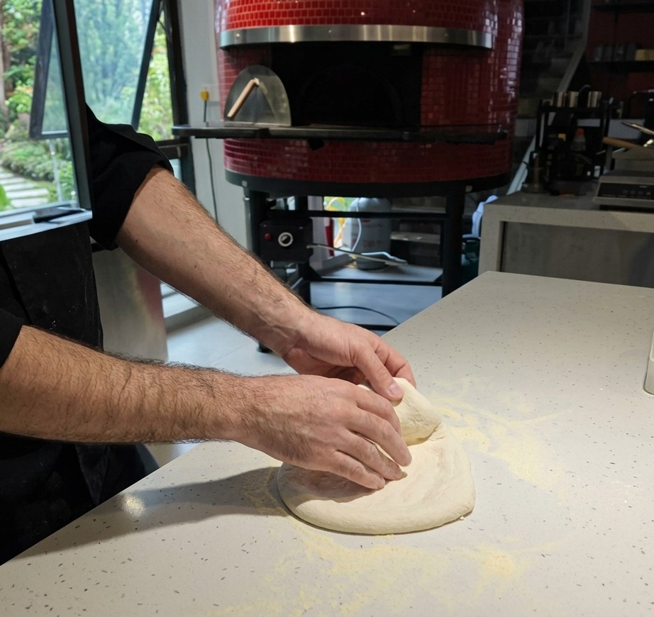 Primer plano de unas manos estirando la masa cruda de pizza sobre una encimera cubierta de harina.