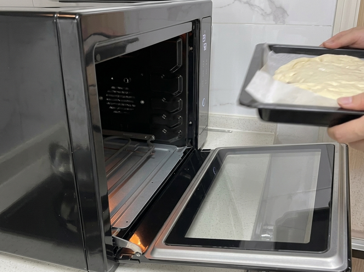 Unas manos introducen una bandeja de horno con la masa de pizza en un horno negro abierto.