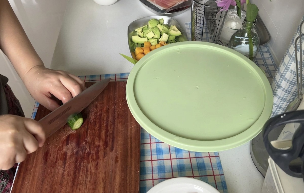 Una persona cortando un pepino fresco en rodajas finas con un cuchillo afilado sobre una tabla de madera.