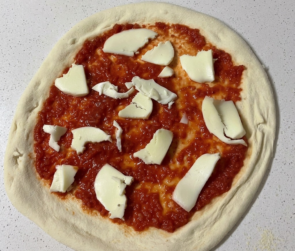 Trozos de queso mozzarella fresco blanco cortados a mano colocándose sobre una base de pizza cubierta con salsa de tomate roja.