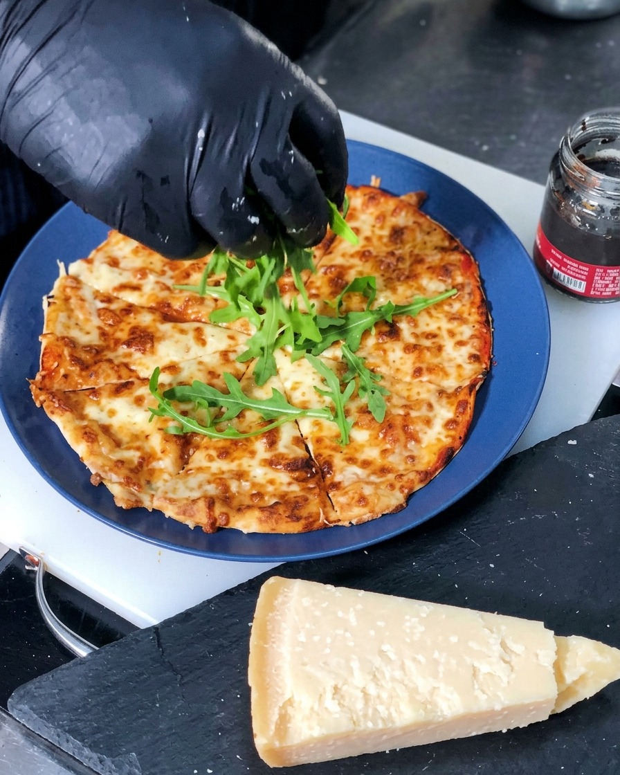 Hojas verdes de rúcula fresca colocadas en el centro de una pizza de queso recién horneada y cortada en porciones.