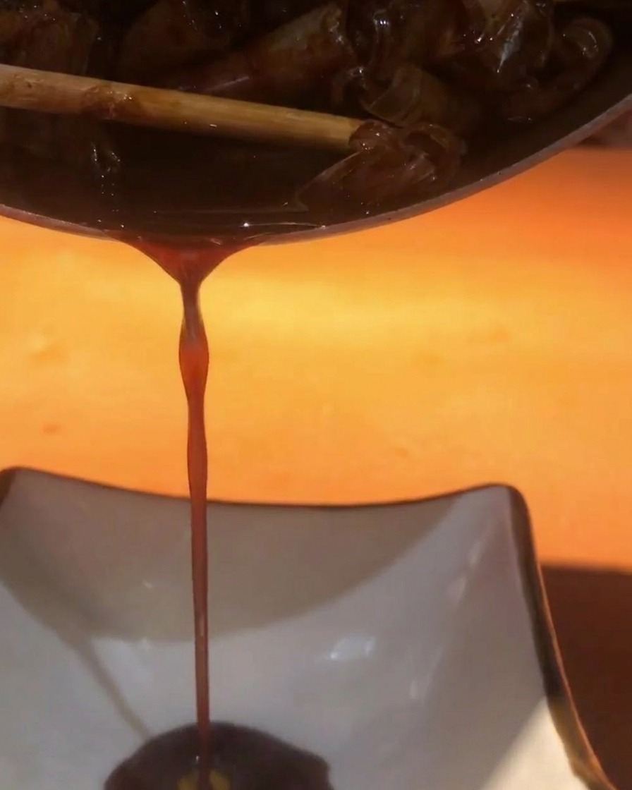 Salsa oscura y sabrosa siendo vertida de una olla a un recipiente cuadrado blanco.