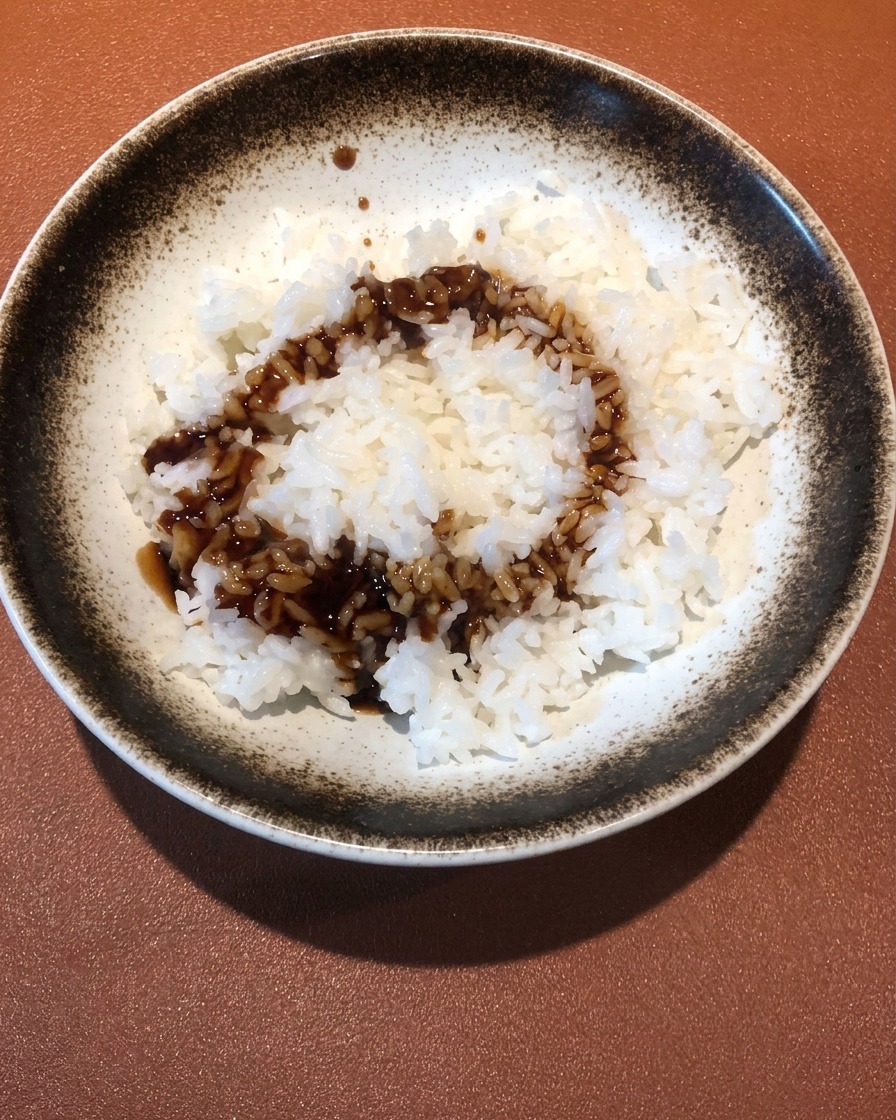 Primer plano de salsa oscura y sabrosa siendo vertida sobre un cuenco de arroz blanco esponjoso.